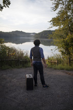 a man standing in front of a lake with a suitcase 