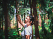 a woman standing in a forest holding a fern 