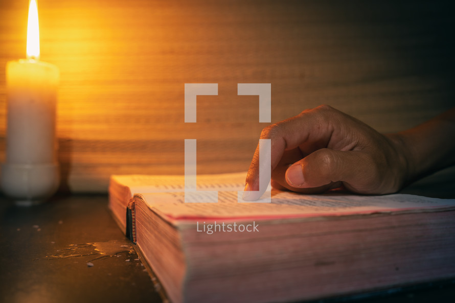 candle light with hands reading bible on wooden table in the night time.