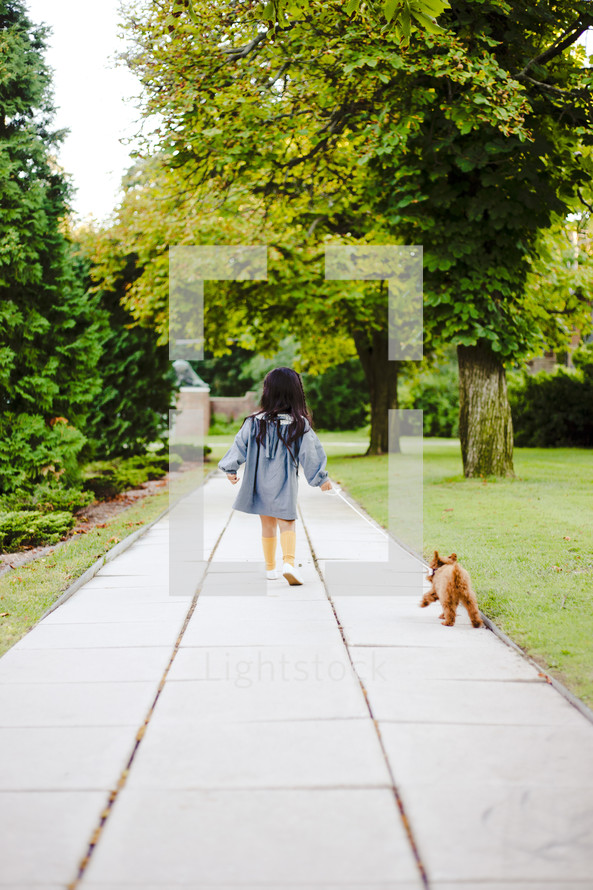 a toddler girl walking a dog on a leash 
