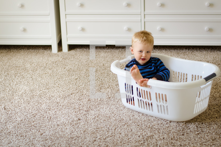 a toddler boy sitting in a laundry basket 
