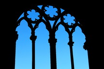 Silhouette of cathedral window frame against a bright blue sky