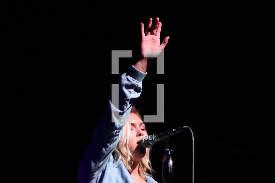 a woman singing into a microphone with a raised hands 