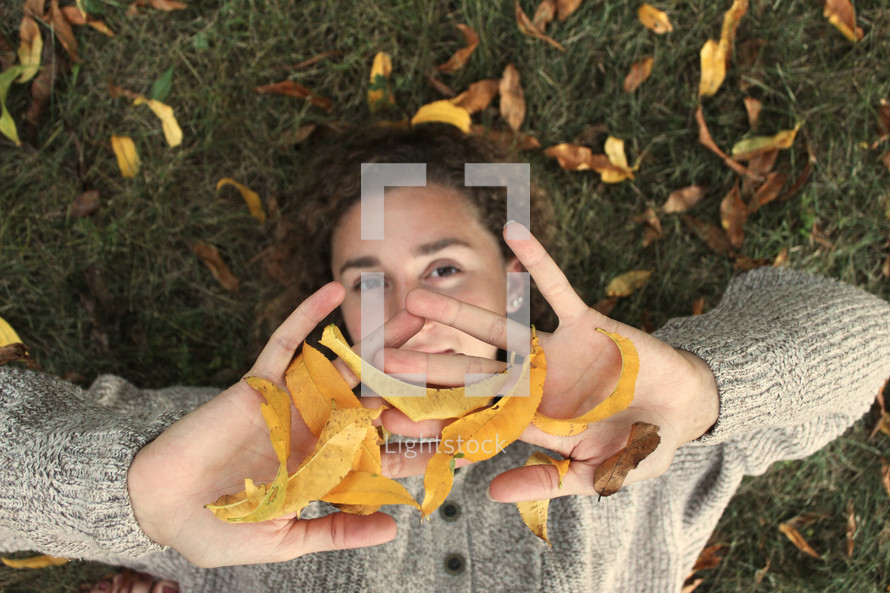 a girl lying in grass playing in fall leaves 