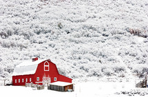 Red barn in snow, with snow-covered hillside in the background.