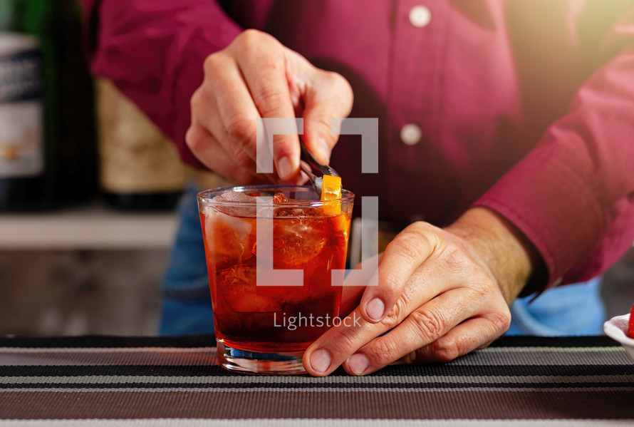 Close-up of a bartender's hands adding a citrus garnish to a chilled cocktail glass