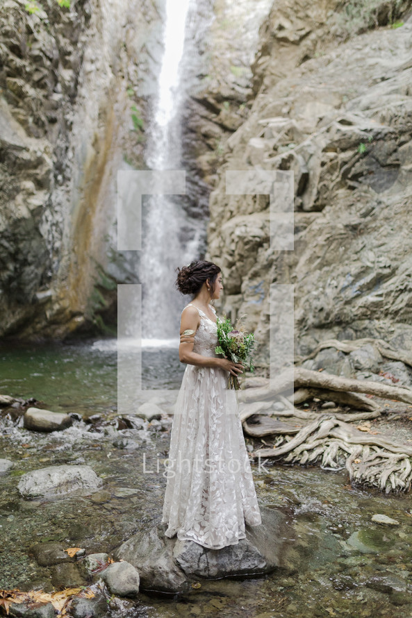 a bride standing in front of a waterfall 