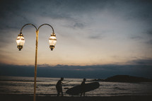 street lamp and man carrying a surfboard at dusk 