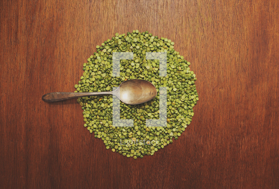 A spoon rests on a circle of split peas on a brown table.