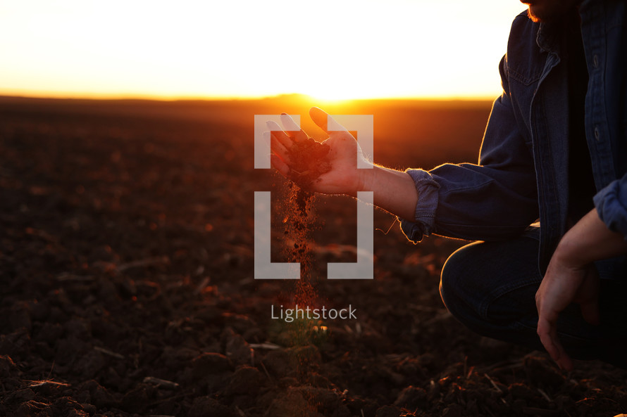 Male farmer's hand holds a handful of dry ground and checks soil fertility and quality before sowing crops on plowed field at sunset. Cultivated land. Concept of organic agriculture and agribusiness.