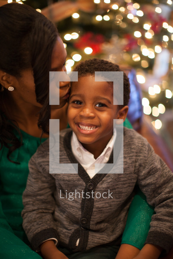 a mother kissing her son in front of a Christmas tree 