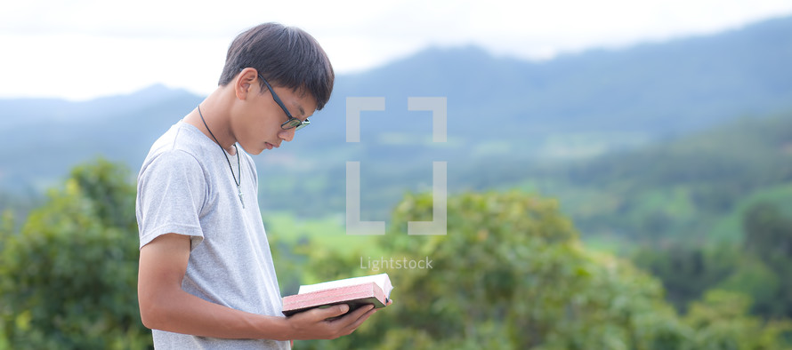 a young man reading a Bible outdoors 
