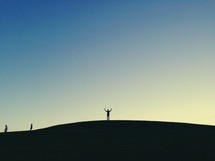 A silhouette of a man with raised hands on a hill. 