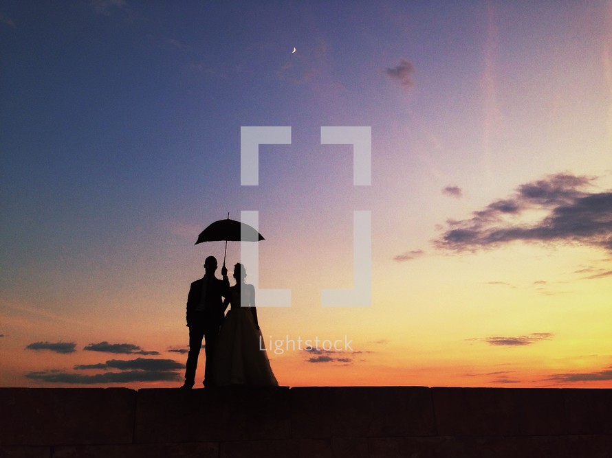 silhouette of a man and woman standing under a parasol. 