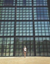 A woman standing in front of a wall of glass windows. 