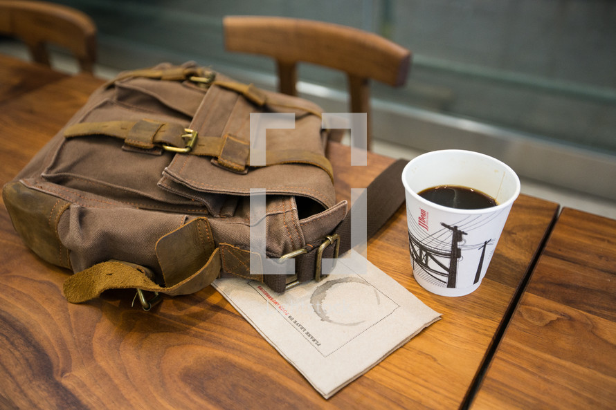coffee cup and backpack on a wood desk 
