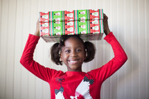 a girl child holding a wrapped Christmas gift over her head 