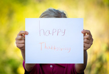 a child holding up a handwritten Happy Thanksgiving sign 