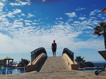 A man standing on a bridge over a swimming pool. 