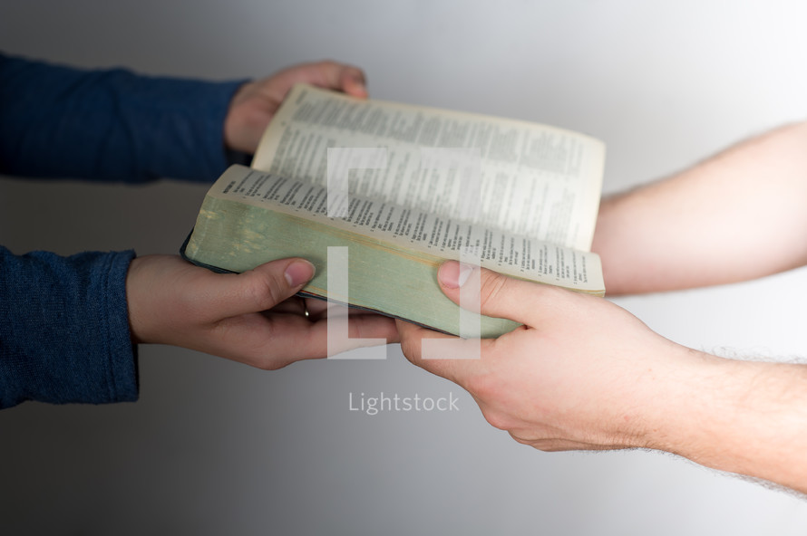 Hands passing a Bible.