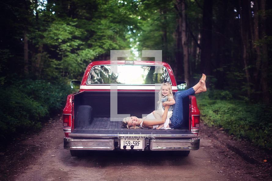 mother and daughter in the back of a truck on a dirt road 
