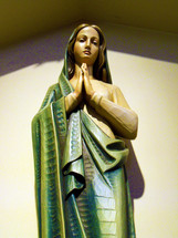 A colorful statue of Mary, the mother of Jesus, wearing emerald green robes and hands clasped together in prayer and worship to God.  