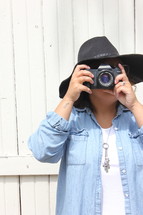 a woman in a hat taking a picture with a camera 
