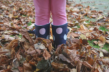 girl with rain boots in fall leaves 