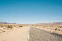 asphalt highway leading through a desert with mountains in the distance