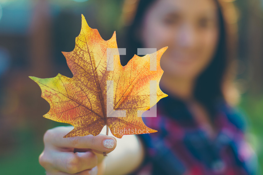 a woman holding a fall leaf 
