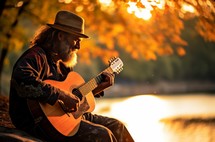 A man in his 45s playing the guitar and singing in a natural park at sunset