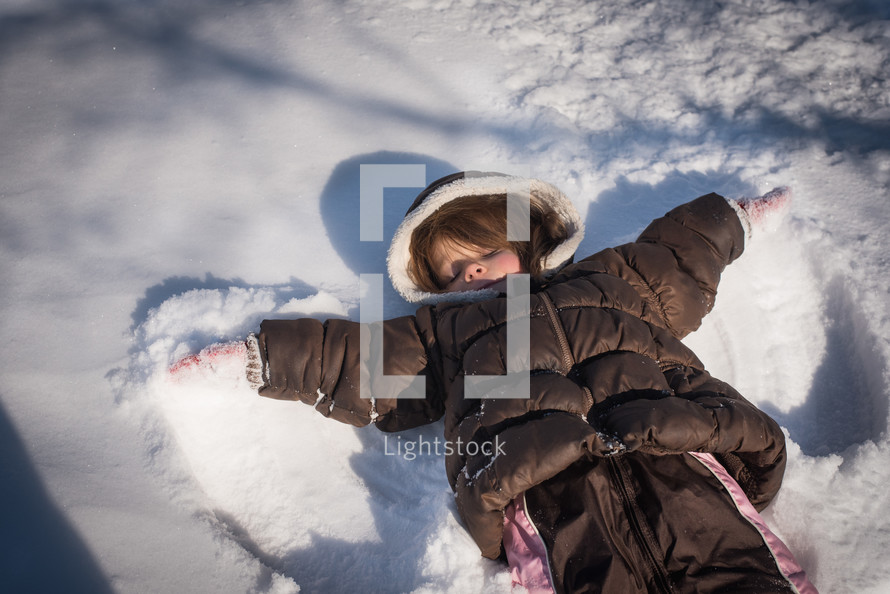 a little girl making snow angels 