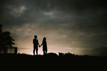 silhouette of a couple holding hands on a shore 
