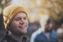 A young man smiling with a yellow beanie on