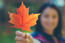a woman holding a fall leaf 