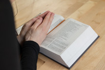 a woman with praying hands over the pages of a Bible 