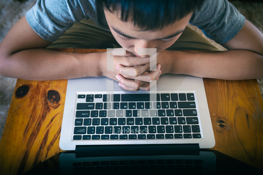 boy praying near a computer 