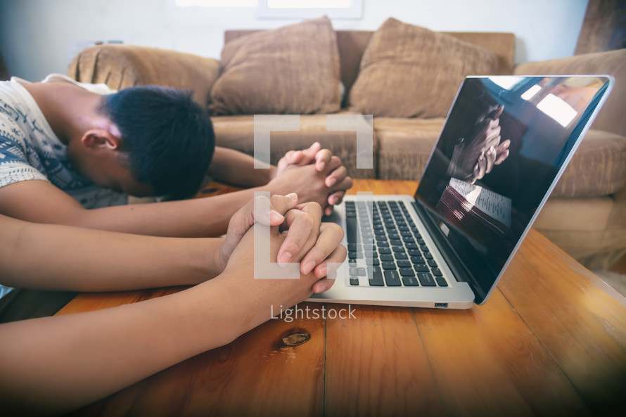 boys praying on a table near a computer 