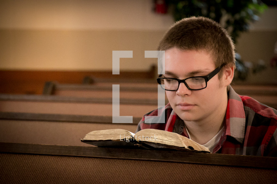 Boy reading his Bible in a church pew.