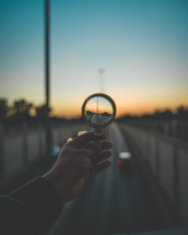 A picture of a magnifying glass held towards the skyline of a highway.