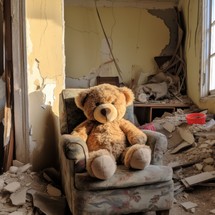 Interior of a room in ruins, with concrete debris scattered everywhere. In the center, there is a large teddy bear sitting on a chair