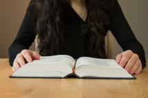 a woman reading a Bible sitting at a desk 