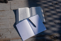Open Bible with notebook and pen on a table outside