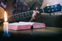 a man playing a guitar with an open Bible nearby 