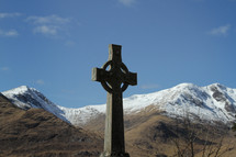 Cross statue outside near snow-covered mountains.