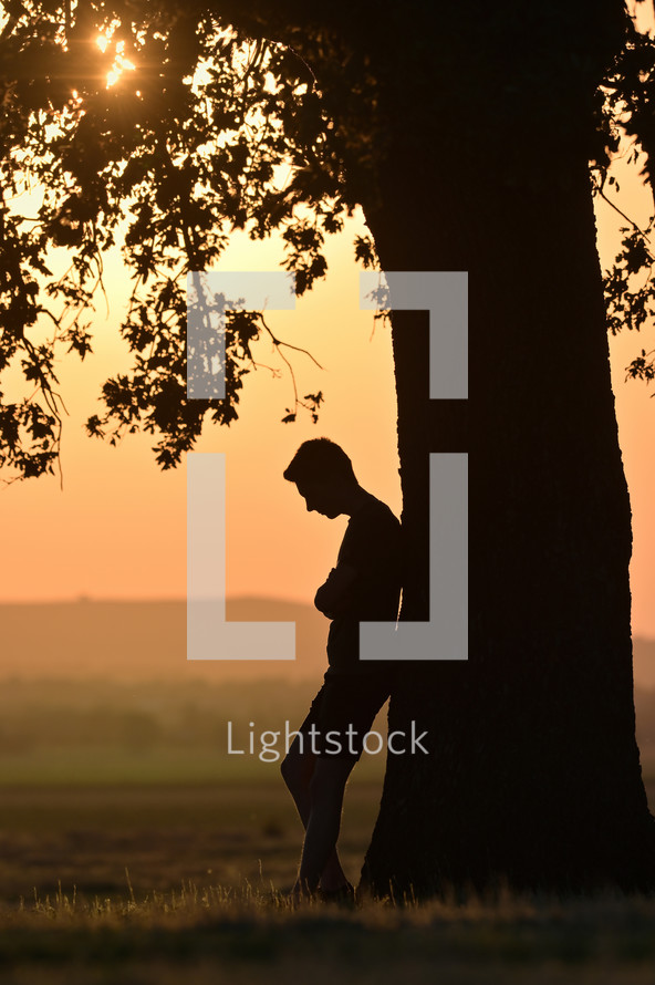 A man praying standing under a tree at sunset 