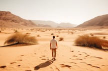 A lone individual wanders through the vastness of a golden desert, surrounded by the tranquility of nature, with footprints trailing behind under the immense open sky