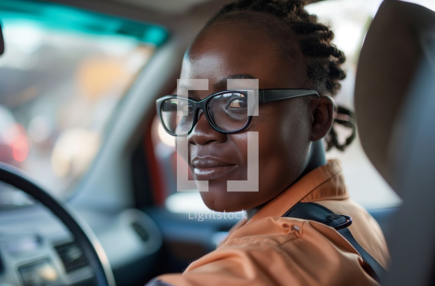 Smiling African American woman wearing glasses and an orange jacket, driving a car