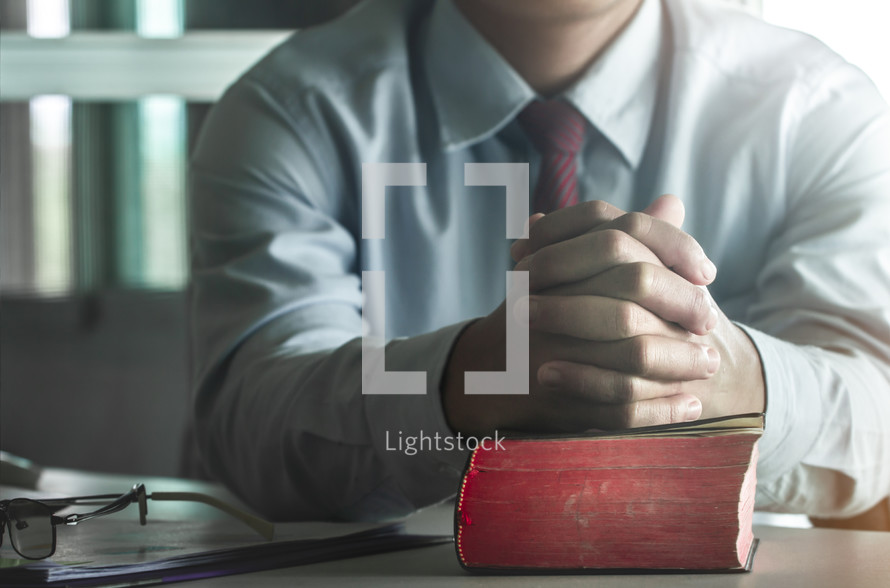 businessman with praying hands on a Bible 