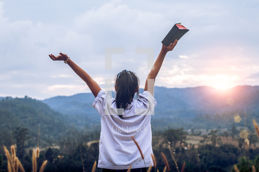Young woman holding and lift up bible to sky outdoors with light sunset background,christian concept.